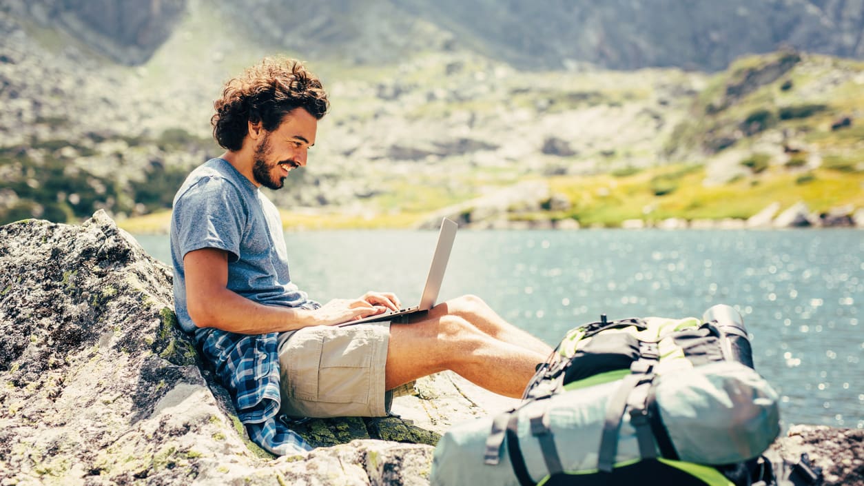 A man is sitting on a rock and using a laptop.