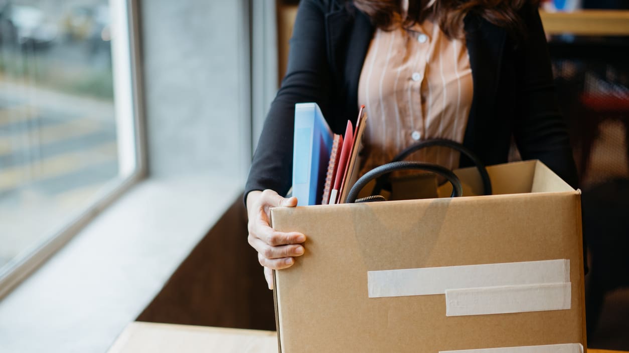 A woman holding a cardboard box full of office supplies.