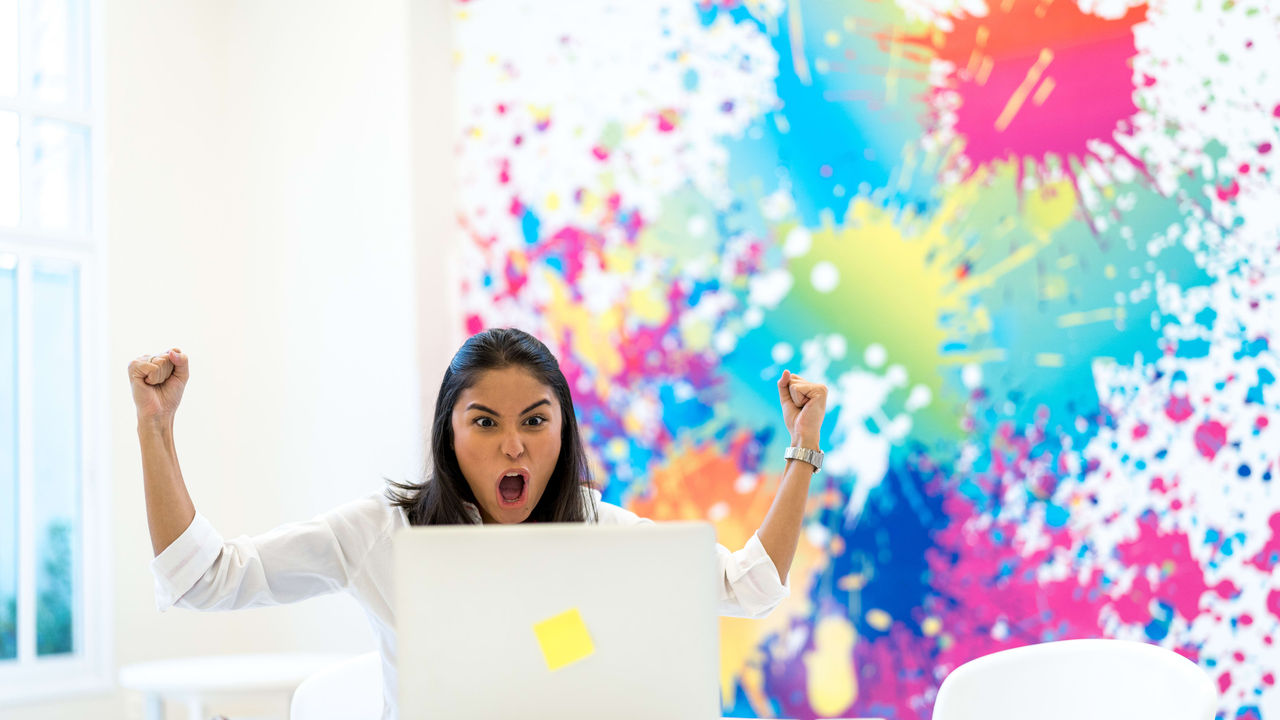 A woman with a laptop in front of a colorful wall.