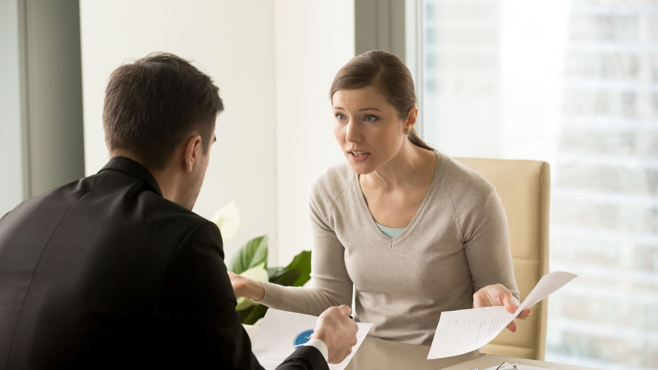 A man and woman talking at a desk in an office.