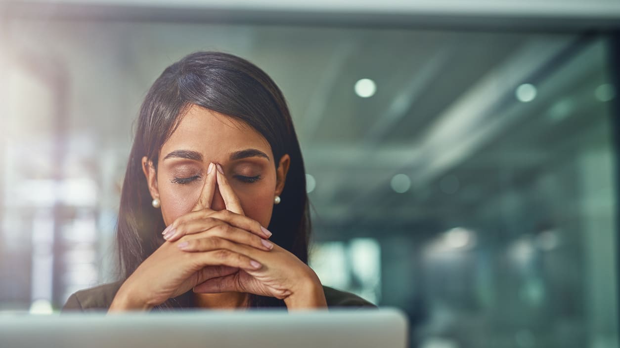 A business woman covering her nose with her hand in front of a laptop.