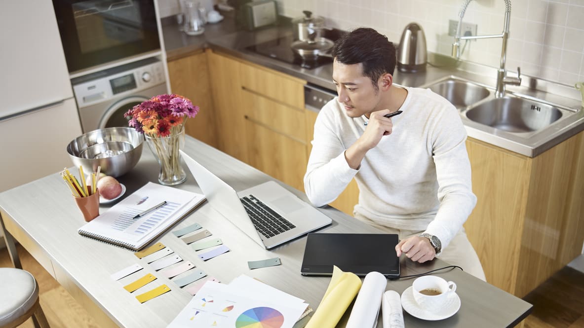 A man working on a laptop in a kitchen.