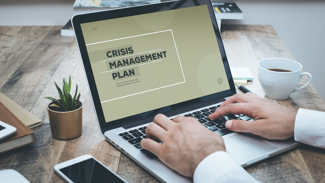 A man working on a laptop with the word crisis management plan on it.