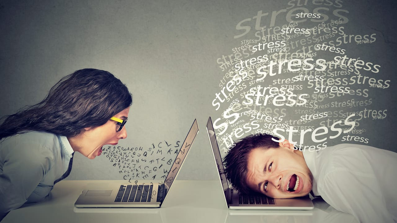 A man and a woman with stress words on their laptops.