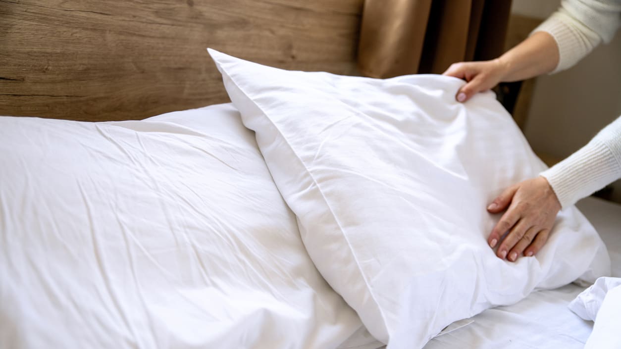 A woman is putting pillows on a bed.