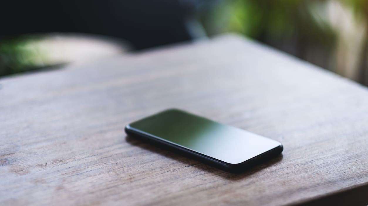 A black smartphone sitting on a wooden table.