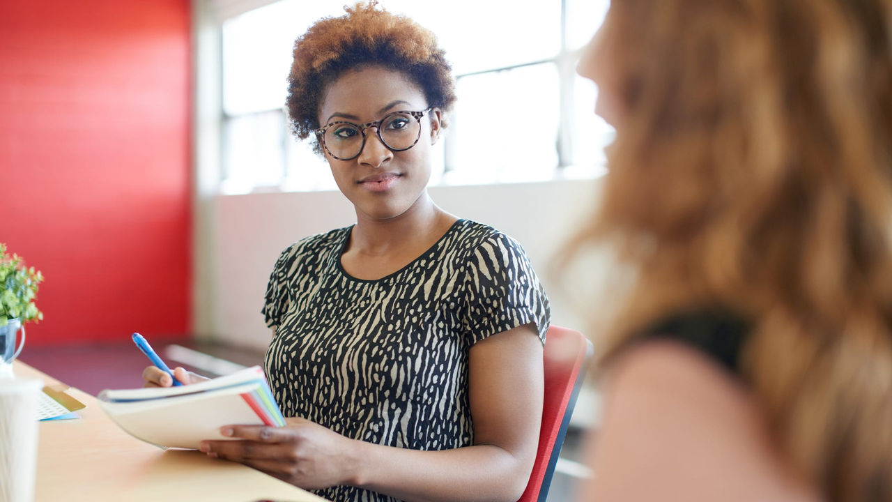 Two women sitting at a table talking to each other.