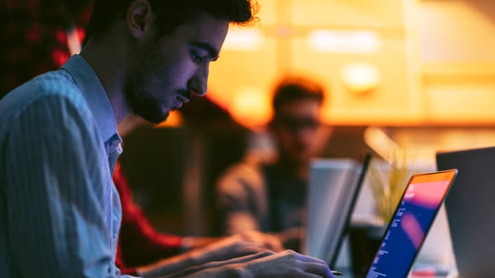 A man is working on a laptop in front of a group of people.