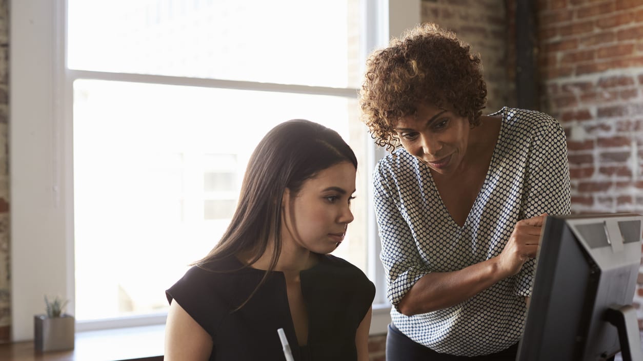 Two women working on a computer in an office.