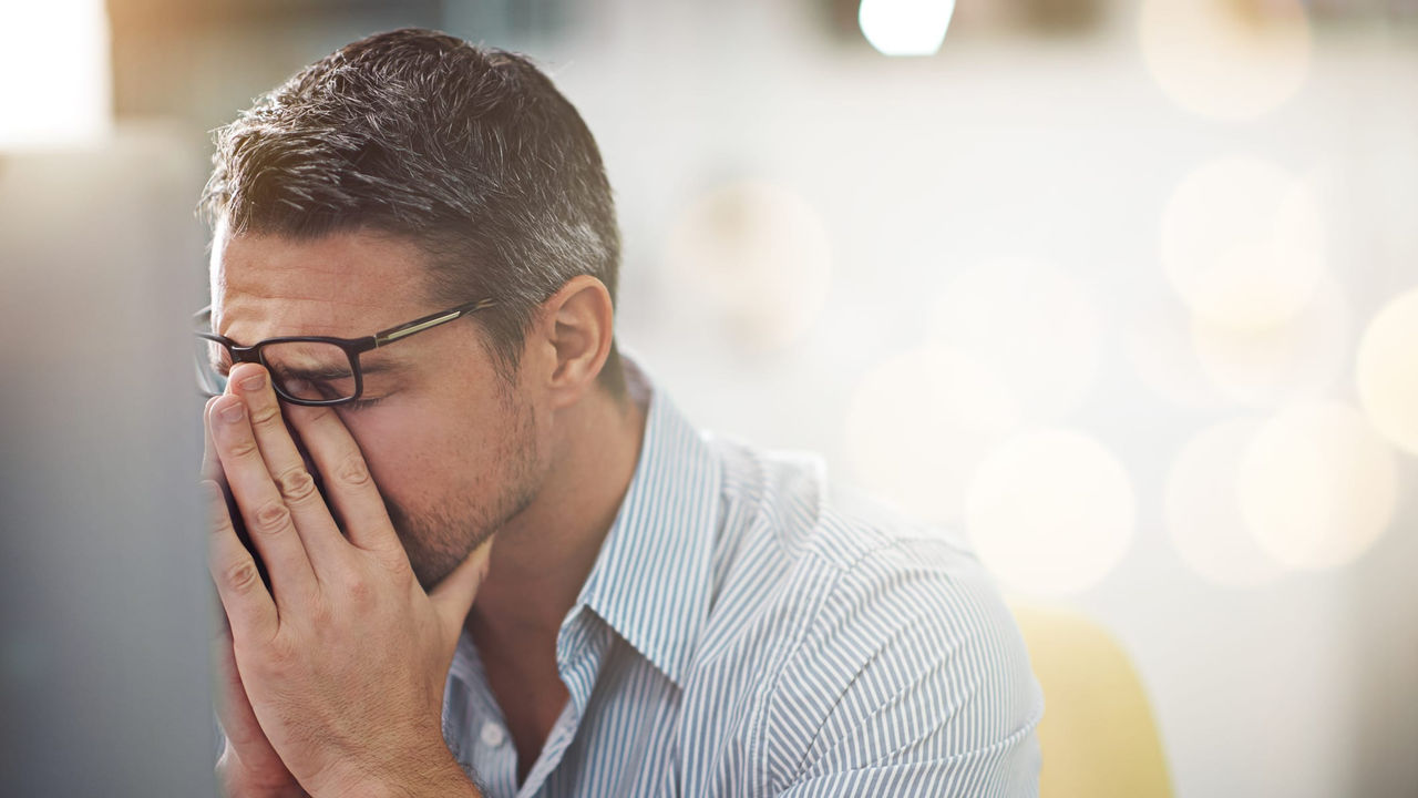 A man covering his face in front of a computer screen.