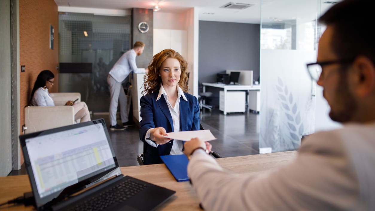 A woman is handing a business card to a man in an office.