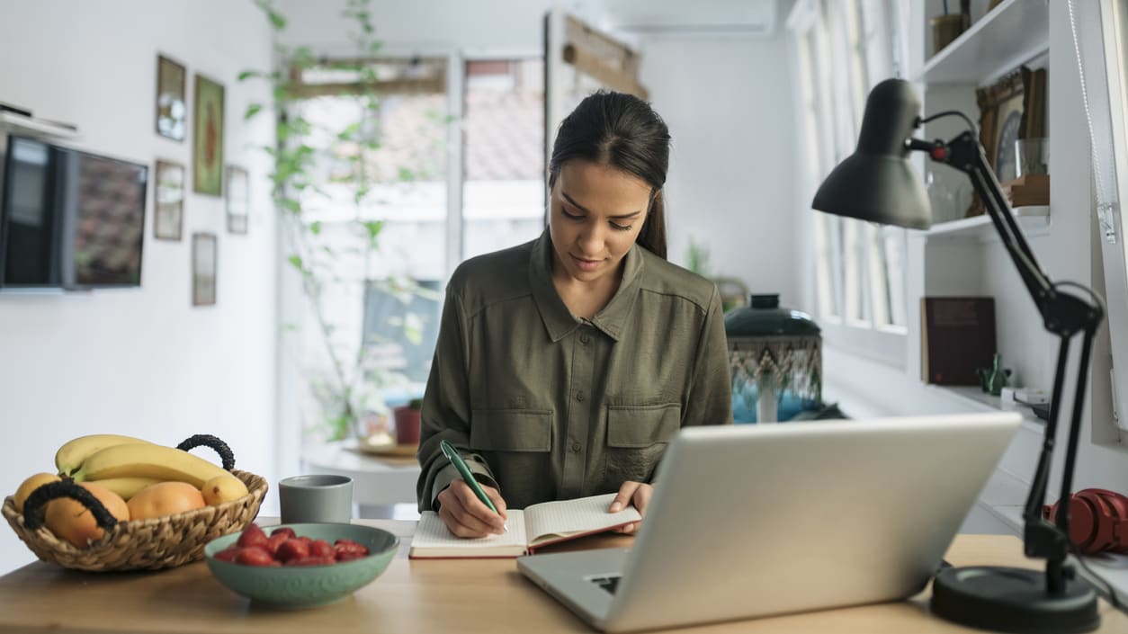 A woman working at home with a laptop and fruit.