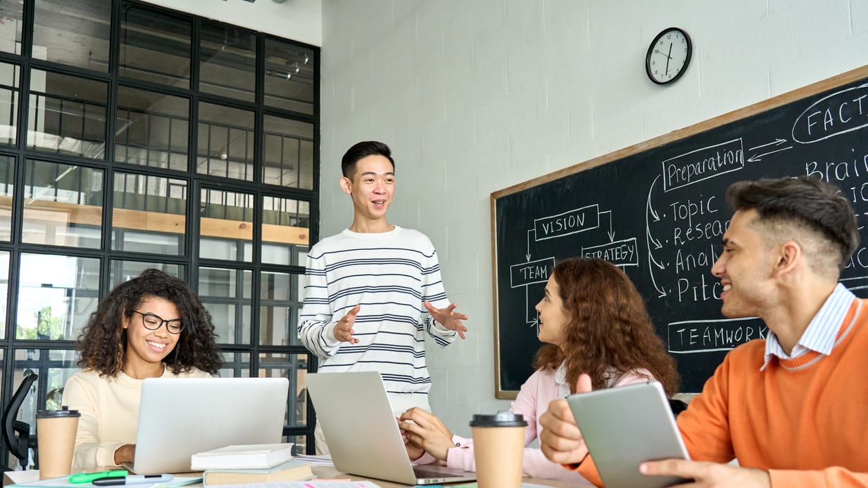 A group of people sitting around a table with laptops in front of them.