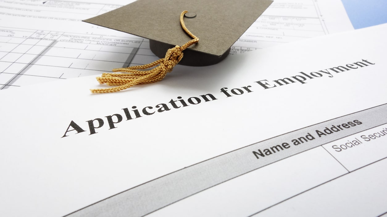 An application for employment is sitting on top of a graduation cap.