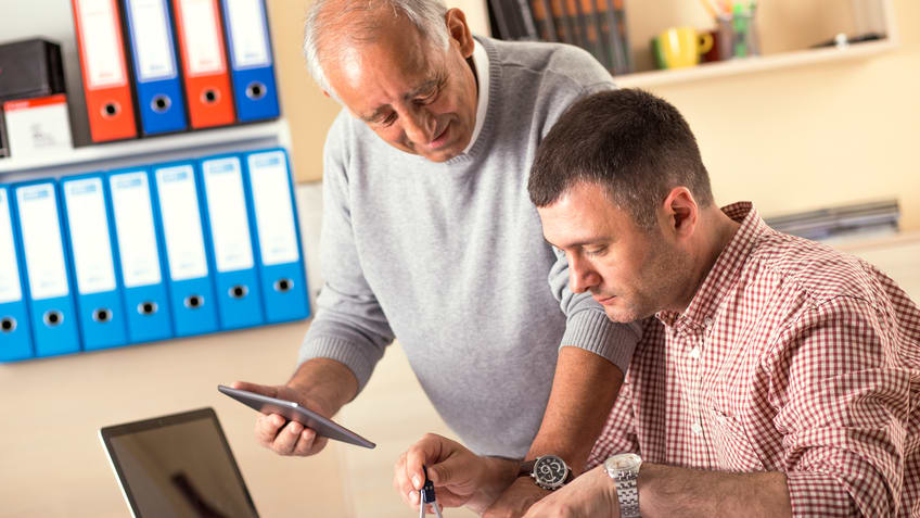 Two men working on blueprints in an office.