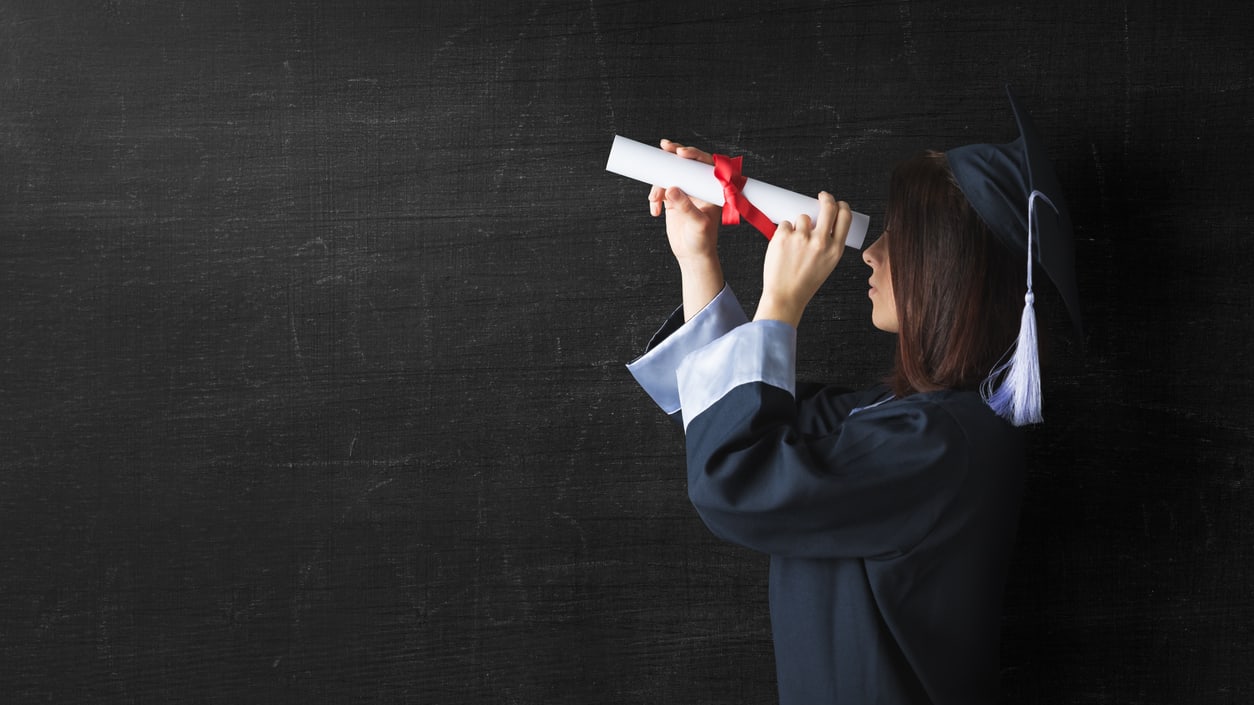 A woman in a graduation gown looking through a diploma.