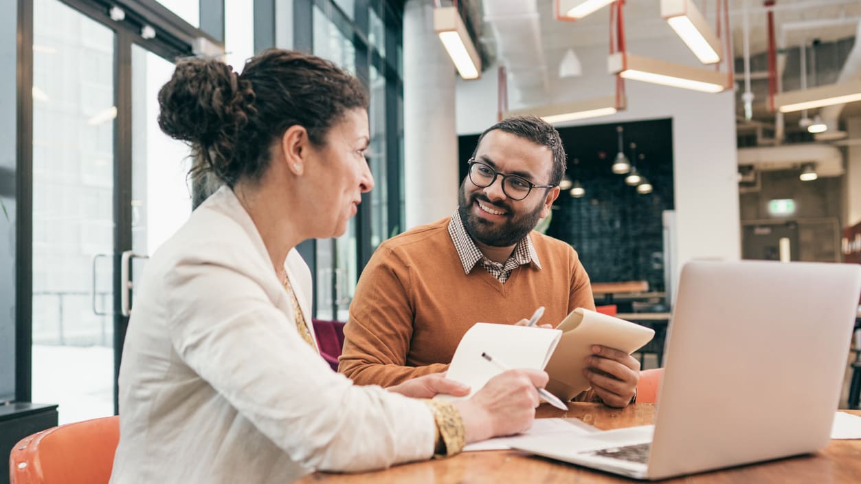 Two business people talking at a table in an office.