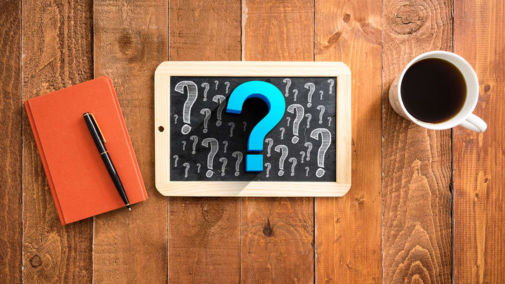 A tablet with question marks on it and a cup of coffee on a wooden table.