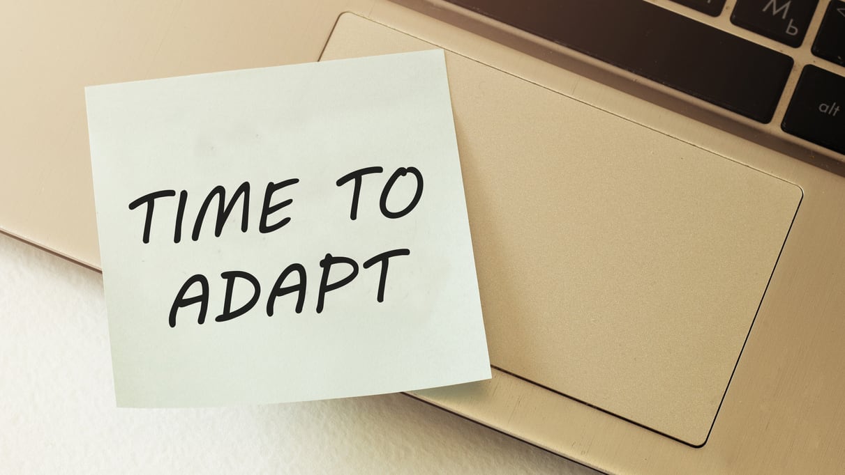 A note with the word time to adapt on top of a laptop.