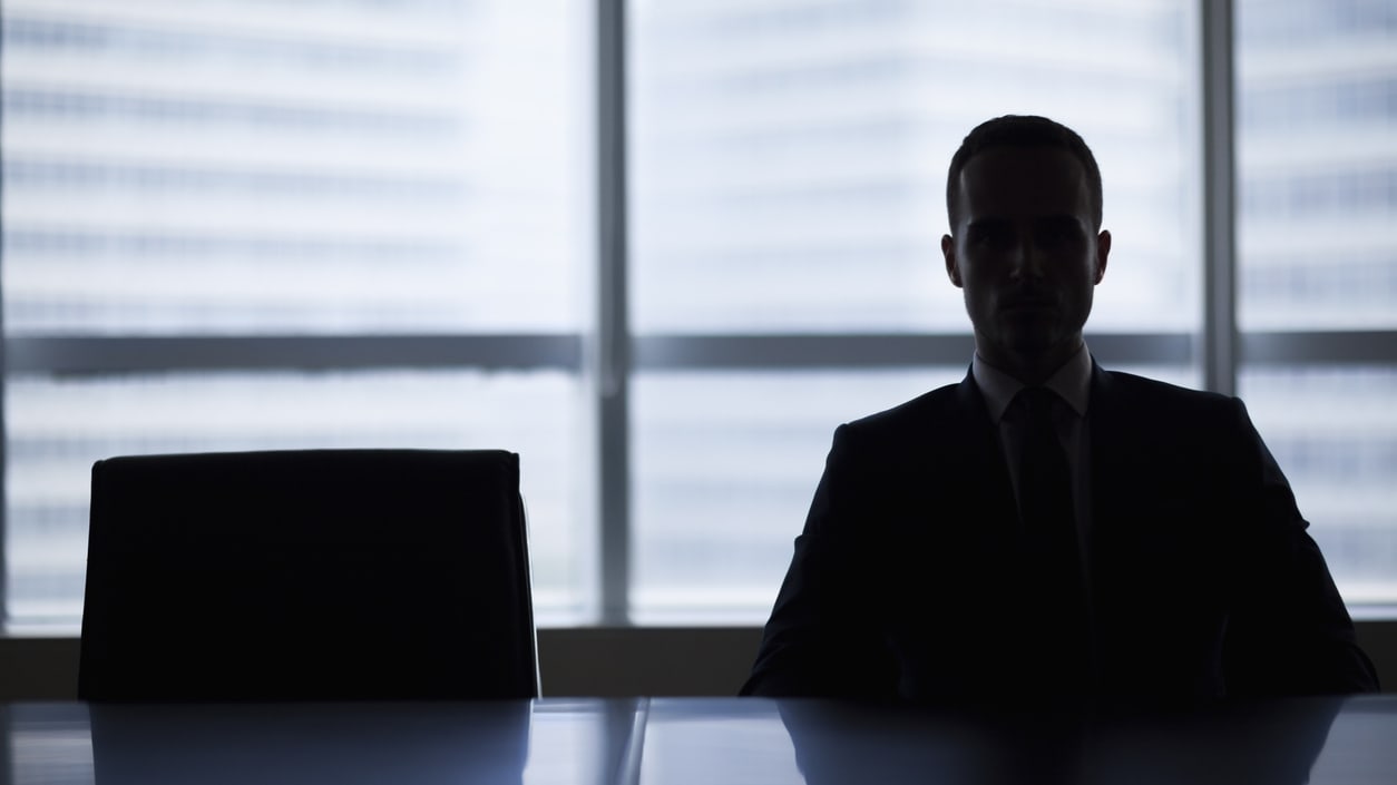 A silhouette of a businessman sitting at a table in front of a window.