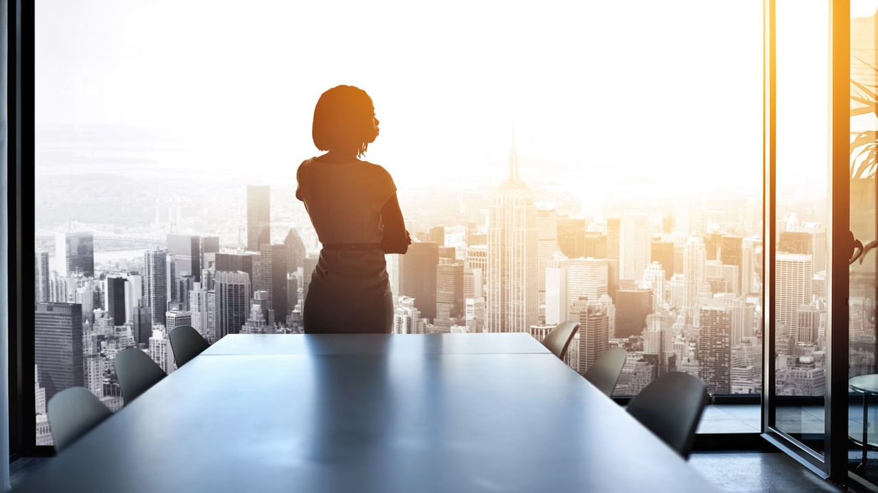 A silhouette of a woman standing in front of a table with a view of a city.