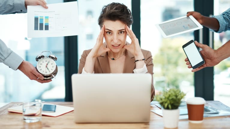 A woman sitting at a desk with a laptop, phone, and other things around her.