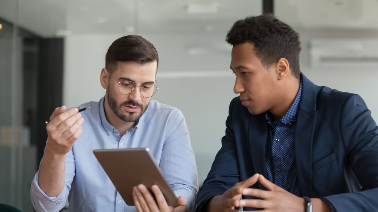 Two businessmen looking at a tablet while sitting at a table.