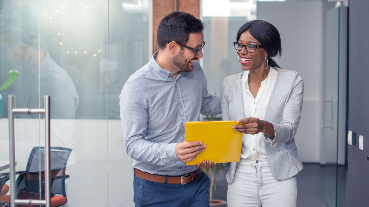 Two business people looking at a yellow folder in an office.