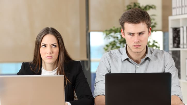 A man and woman sitting at a desk with laptops in front of them.