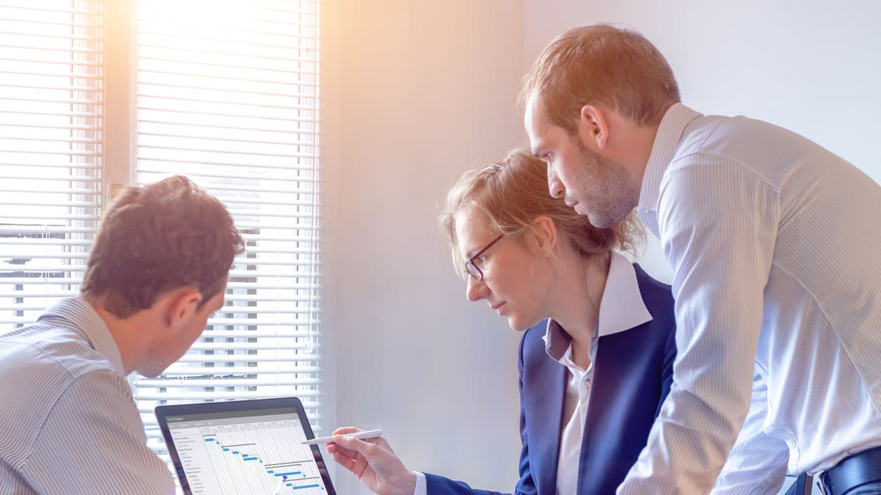 Three business people looking at a laptop screen.