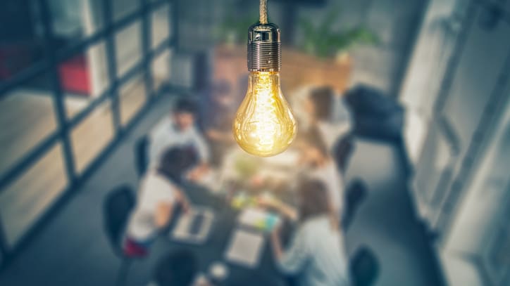 A group of people sitting around a table with a light bulb hanging above them.