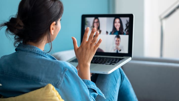 A woman sitting on a couch watching a video conference on her laptop.