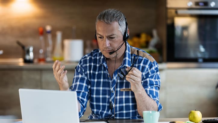 A man working on a laptop while wearing a headset.