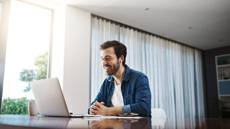 A man sitting at a desk with a laptop in front of a window.