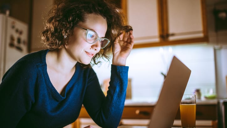 A woman is working on her laptop in the kitchen.