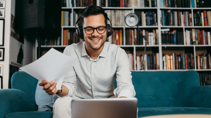 A man sitting on a couch with headphones and a laptop.