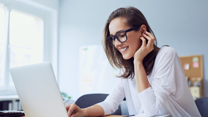 A woman wearing glasses is working on a laptop.