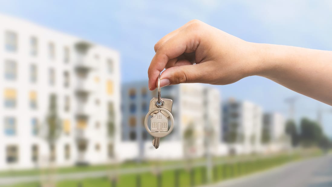 A hand holding a key to a house in the background.