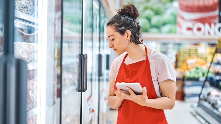 A woman in an apron is using a tablet in a grocery store.