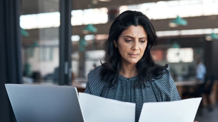 A business woman is looking at a sheet of paper while sitting at a desk.