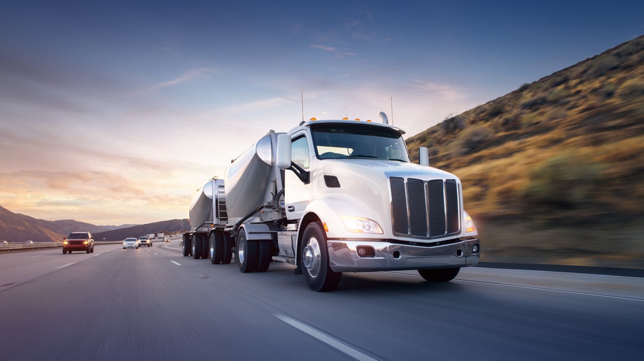 A semi truck driving down a highway at sunset.