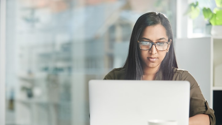 A woman wearing glasses is using a laptop.