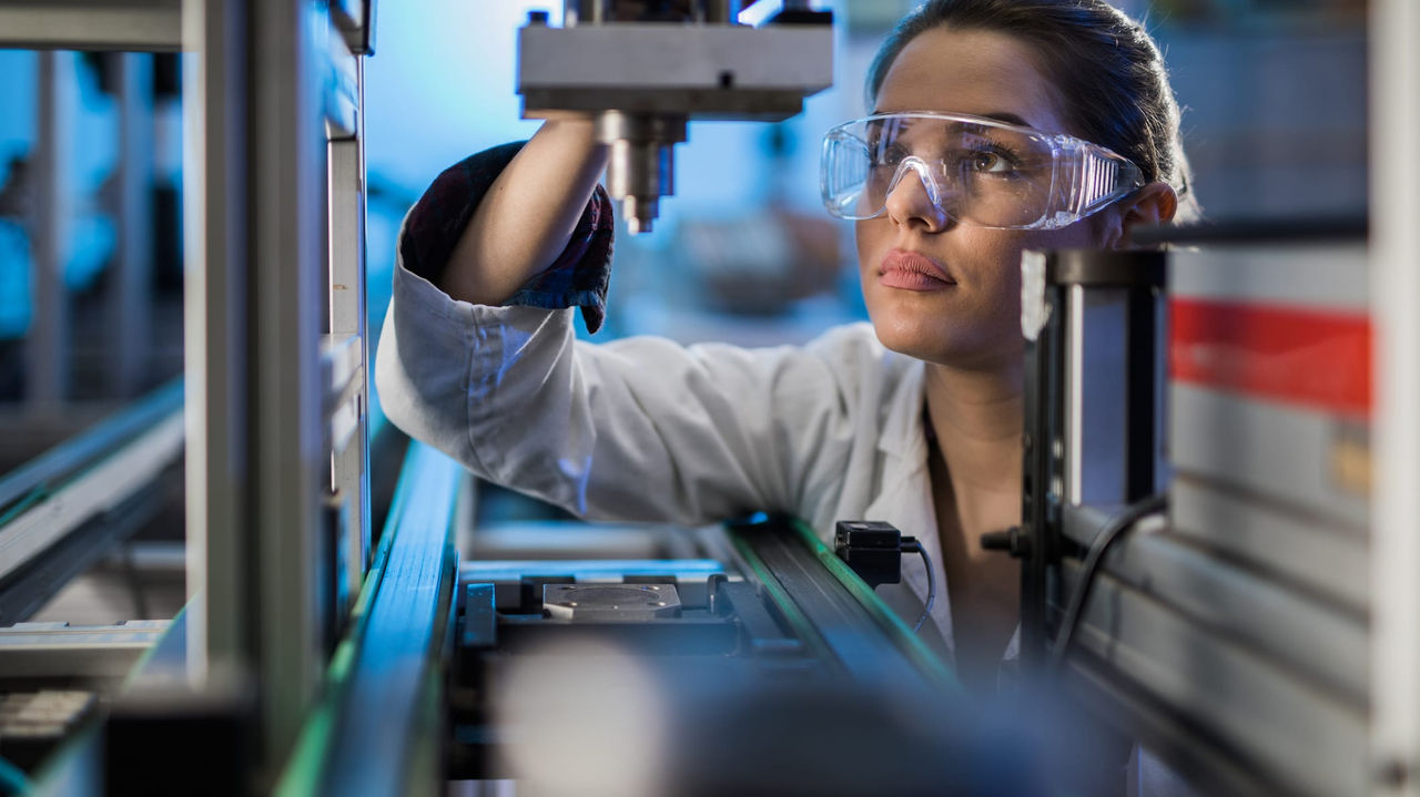 A woman wearing safety goggles and looking at a machine.