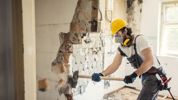 A man is hammering down a wall in a room.