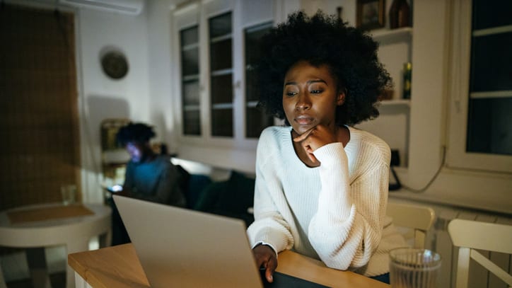 A woman sitting at a table looking at her laptop.