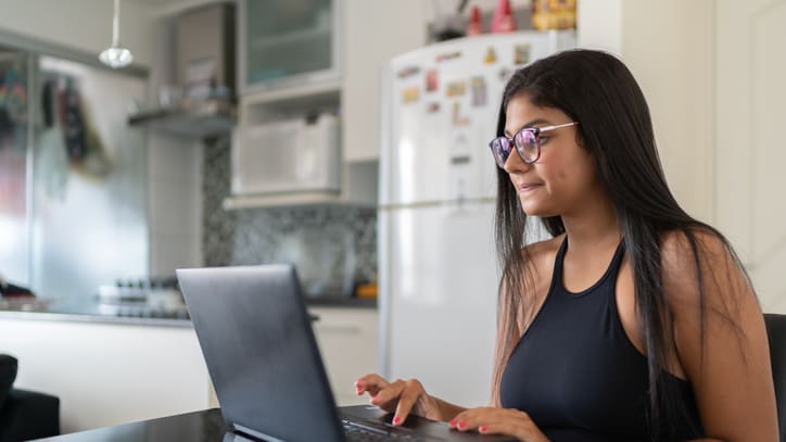 A young woman using a laptop in her kitchen.