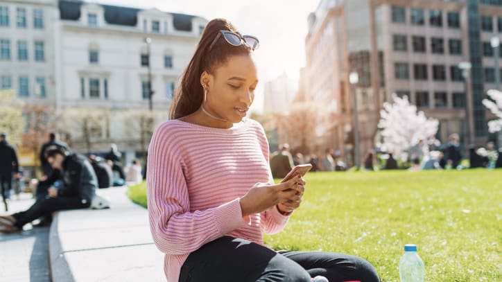 Young african american woman sitting on the ground and using her cell phone.