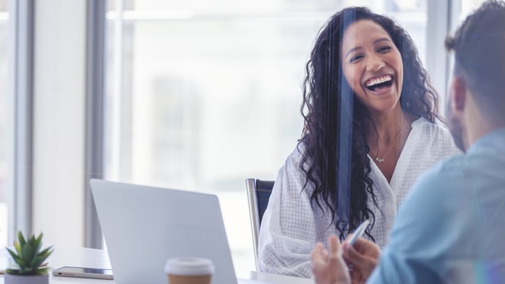 A woman and man laughing at a meeting in an office.