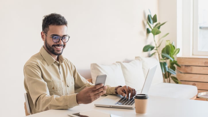 A man sitting at a desk with a laptop and cell phone.