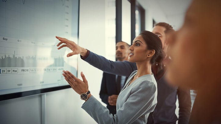 A group of business people pointing at a graph on a screen.